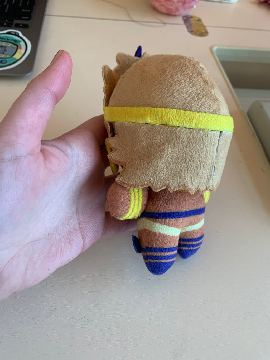 Back view of a  plush toy with golden jewelry and a red square face marking