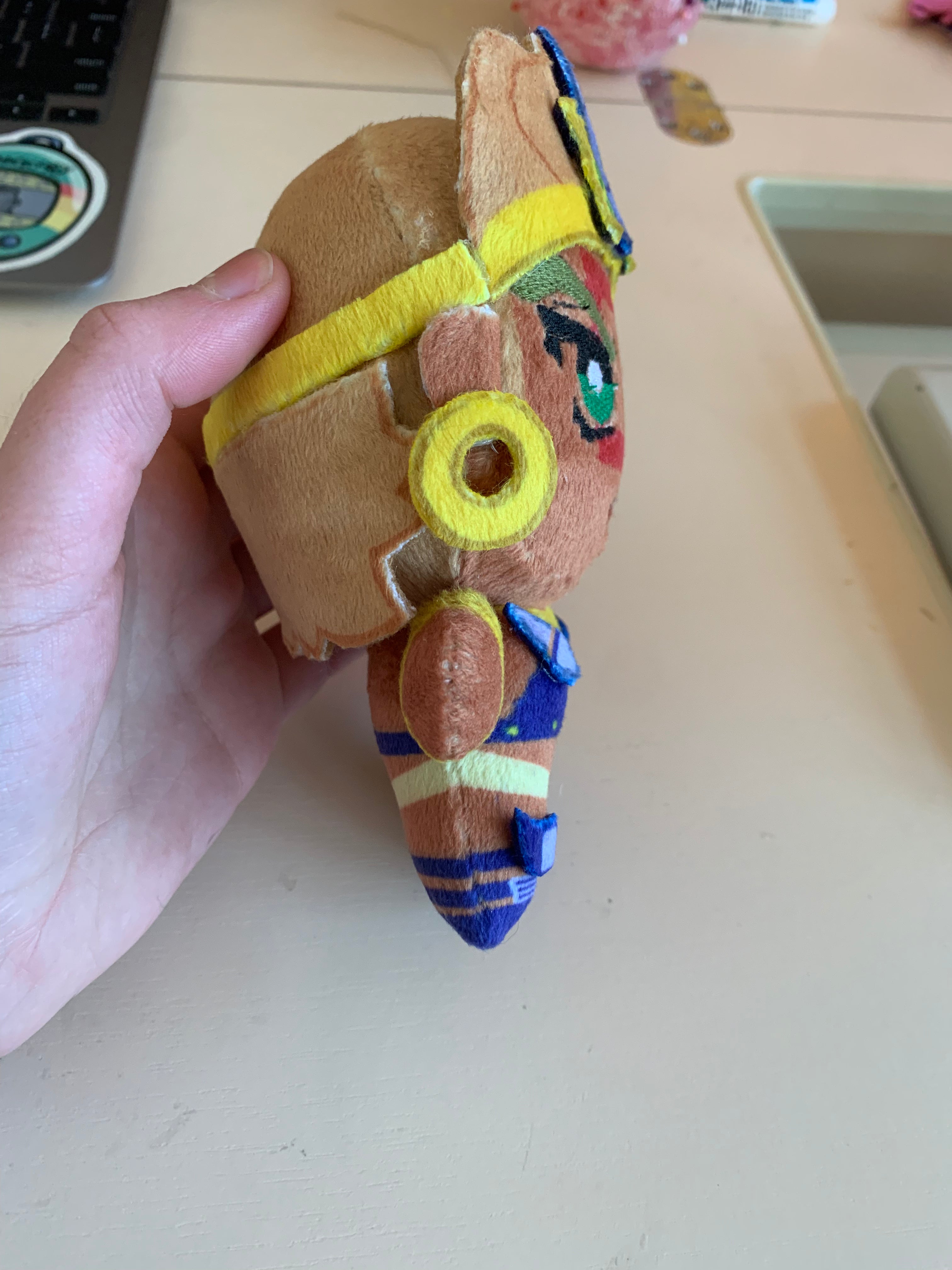 Side view of a plush toy with golden jewelry and a red square face marking