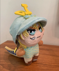 Plush toy with a blue jockey's cap and yellow dinosaur tail standing up on a wooden surface