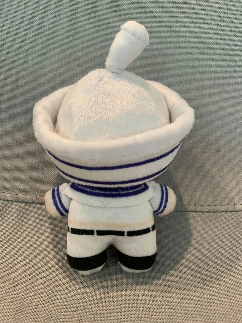 The back of a small plush toy in a sailor outfit on a gray background