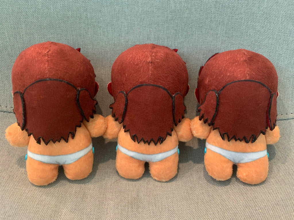 Back view of three plush toys with red hair and white loincloths on a gray background