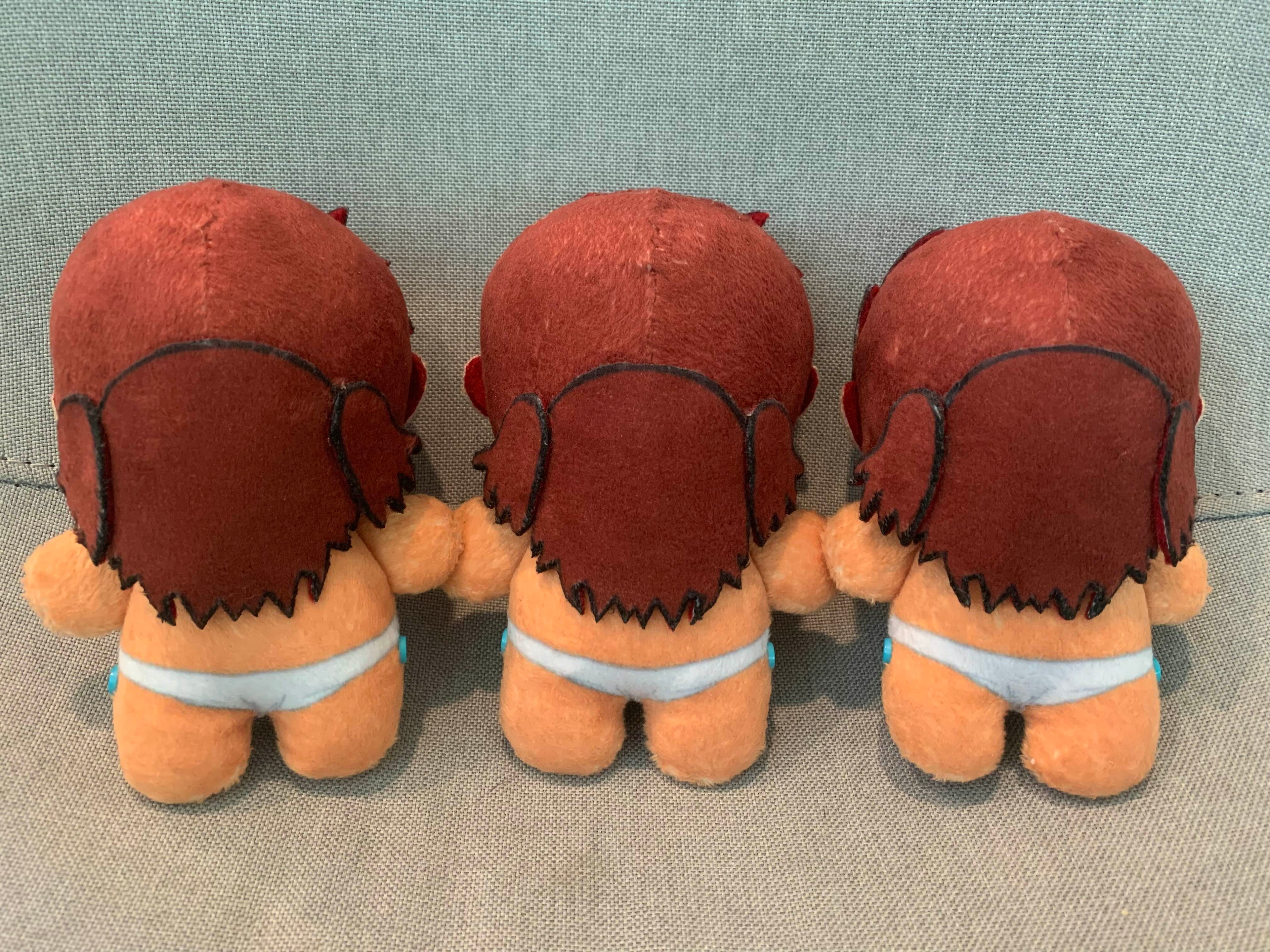 Back view of three plush toys with red hair and white loincloths on a gray background