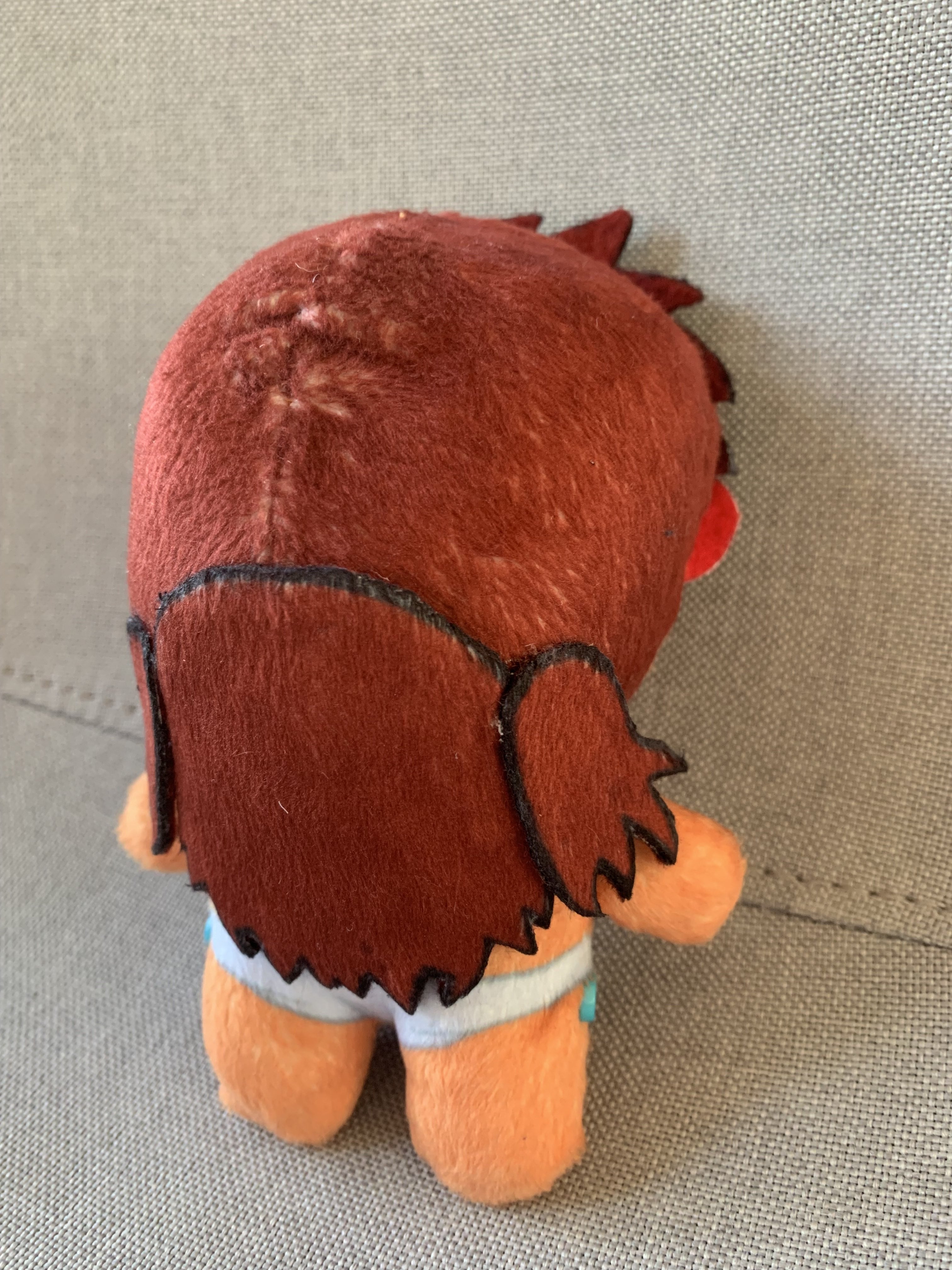 Back view of a plush toy with red hair on a grey background