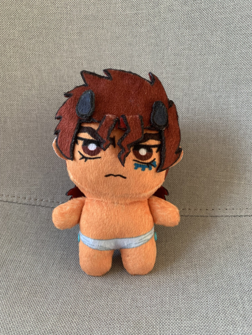 A plush toy with red hair and an angry frown on a grey background