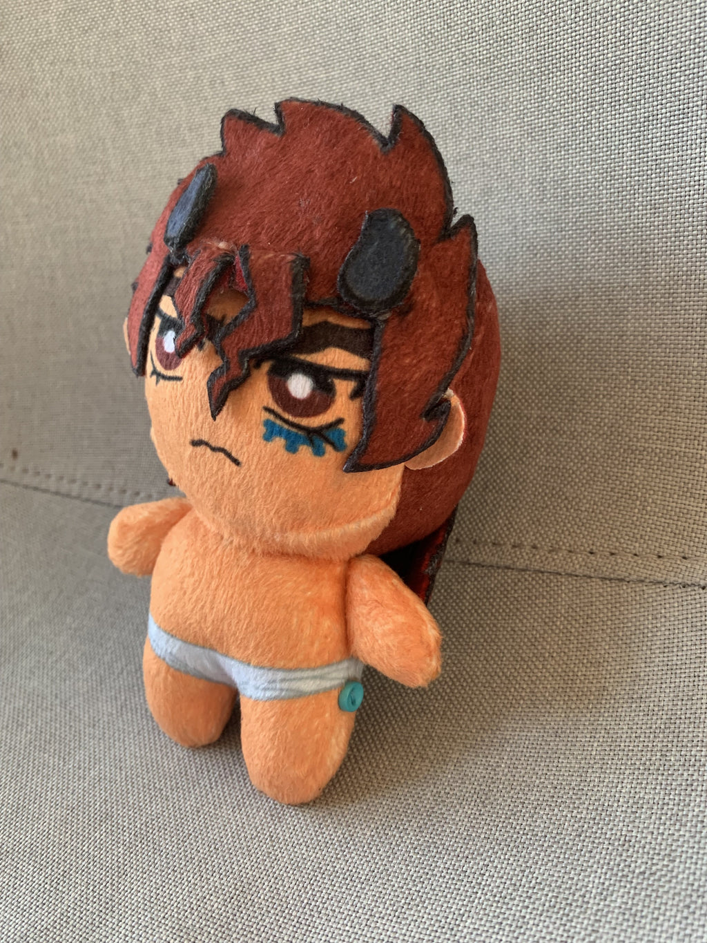 Side view of a plush toy with red hair and an angry frown on a grey background