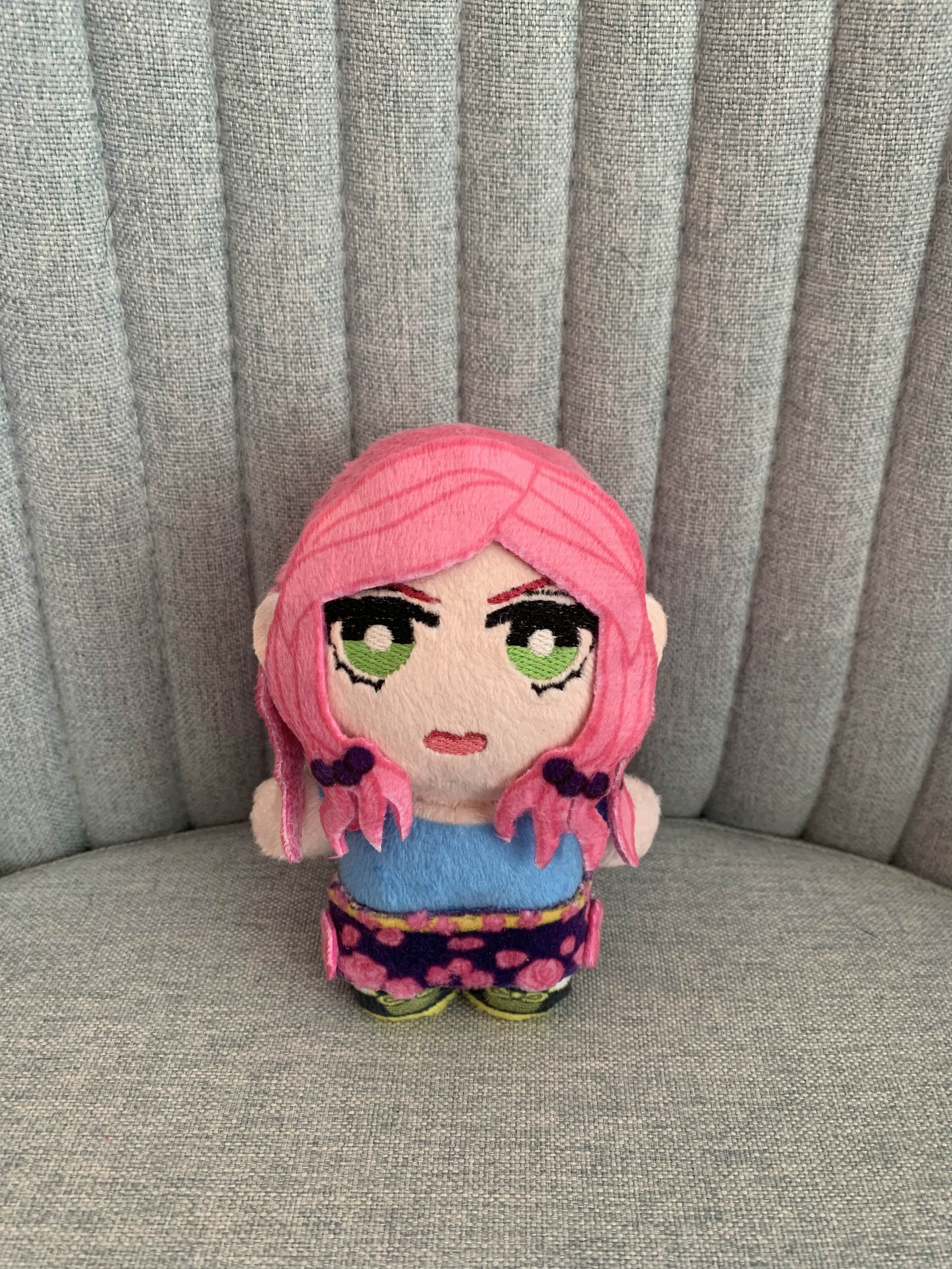 Plush toy with pink hair and green eyes on a gray surface