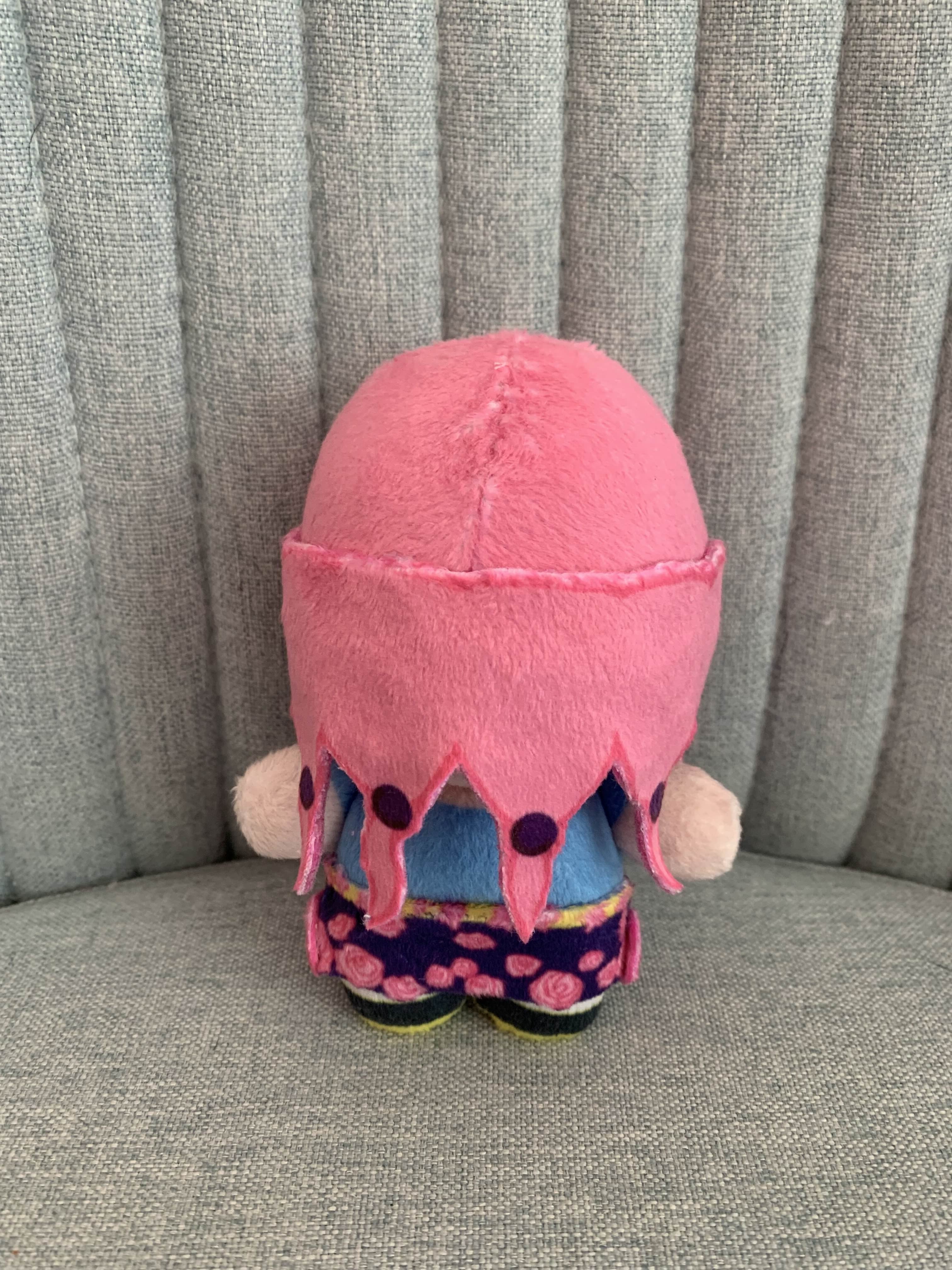 Back view of a plush toy with pink hair and blue shirt on a gray background