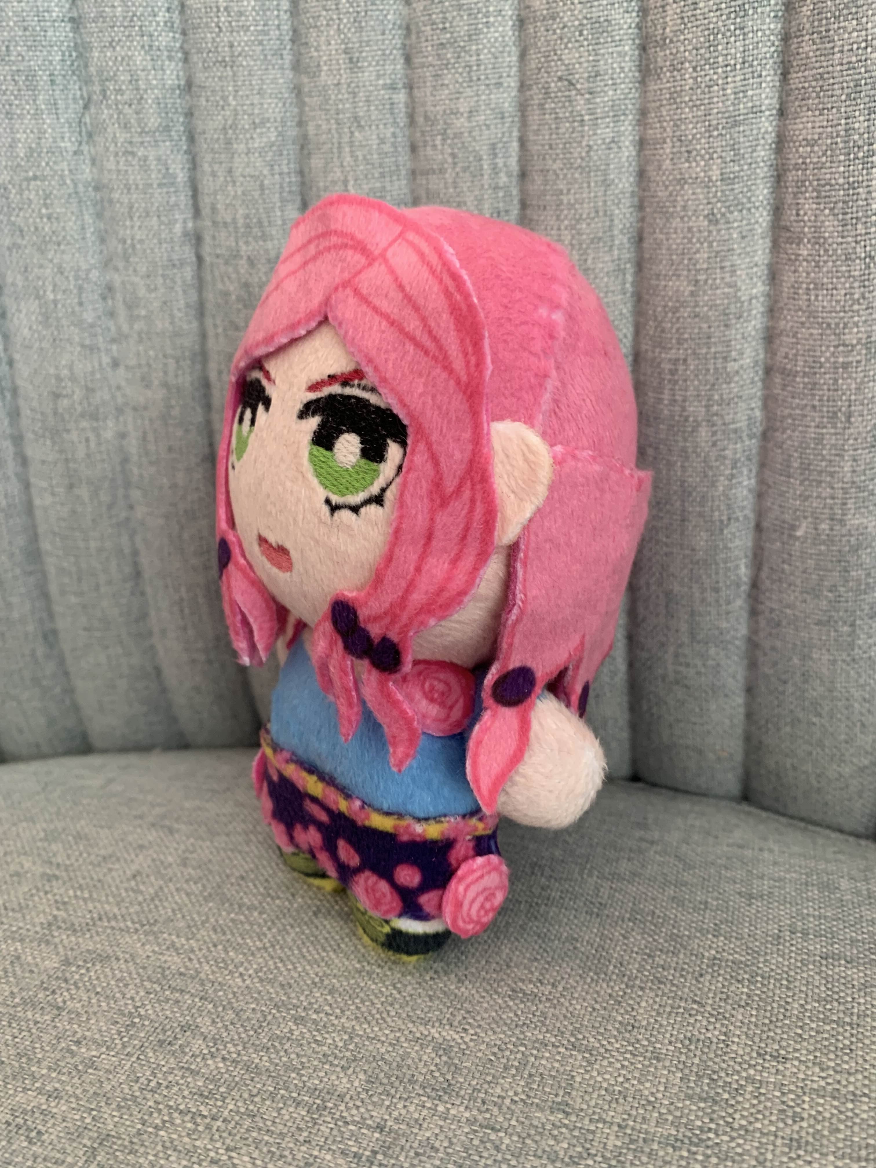 Side view of a plush toy with pink hair and green eyes on a gray surface