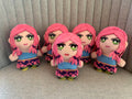 Five identical plush toys with pink hair and green eyes sitting on a gray surface.